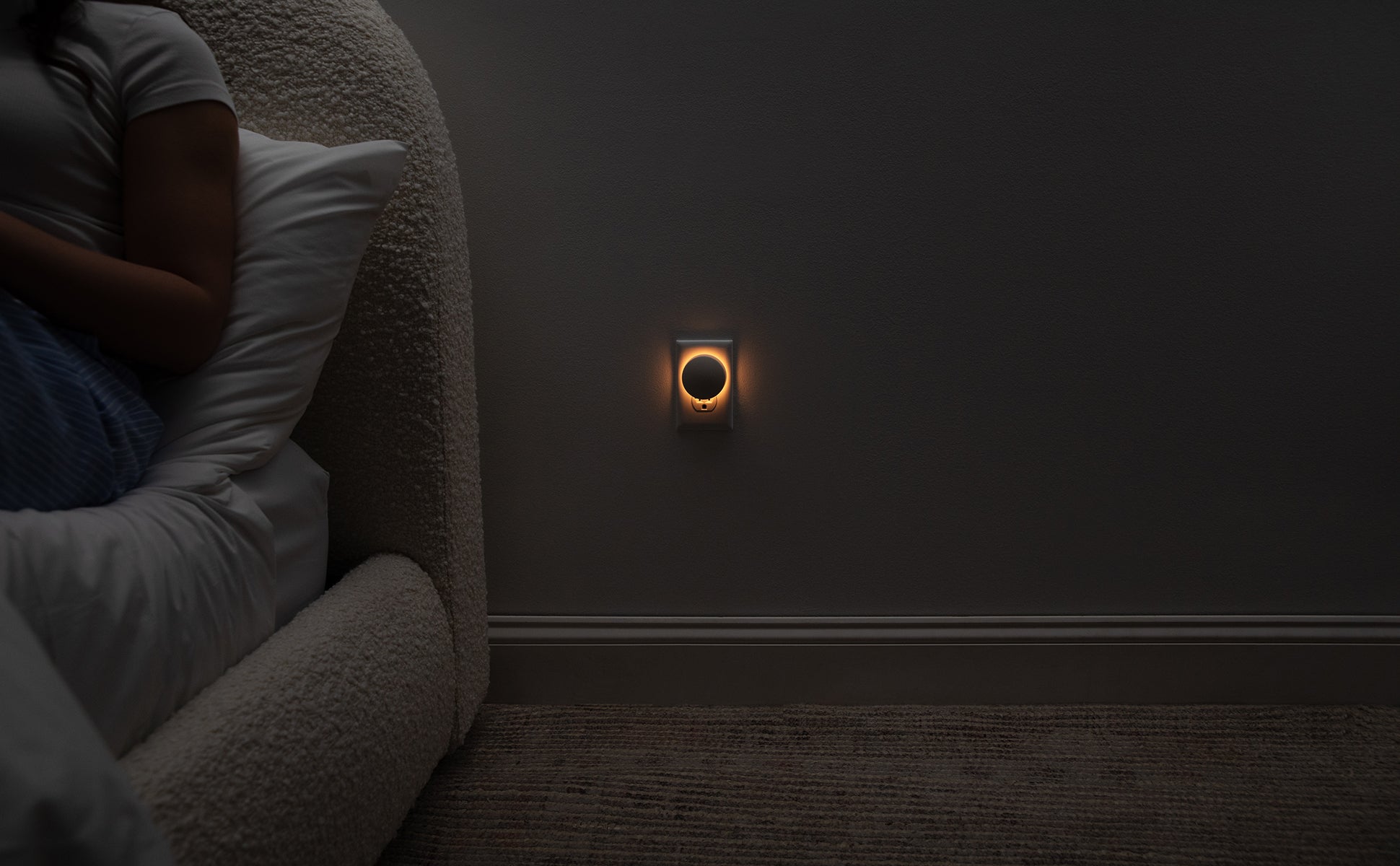Image of the Glow Nightlight turned on next to a bed, emitting a soft, orange glow.