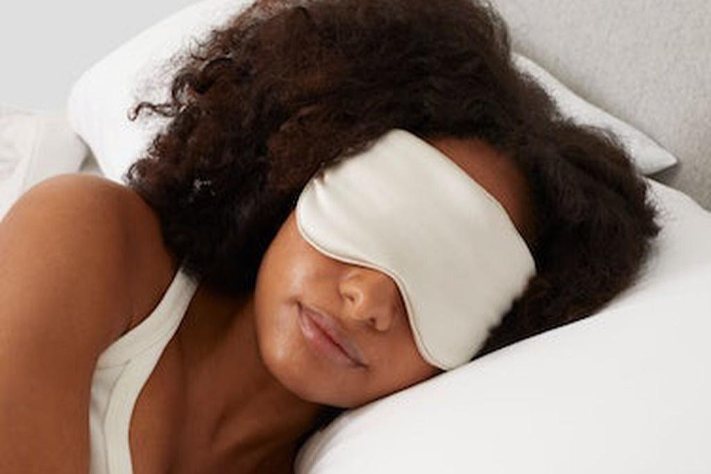 A woman wearing the Silk Sleep Mask, oatmilk, in bed