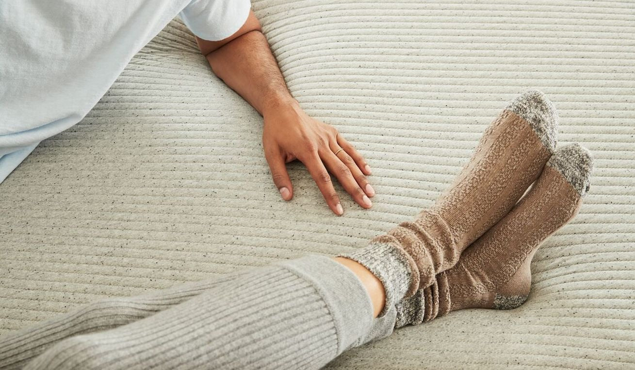 Close-up image of one person's arm and another person's feet resting comfortably on a mattress.