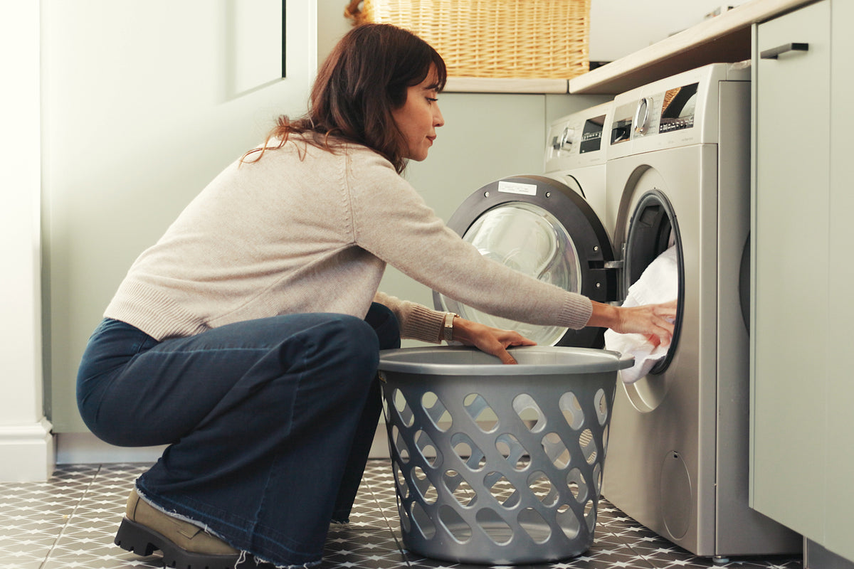 A woman squats down to add or remove garments from a laundry machine.