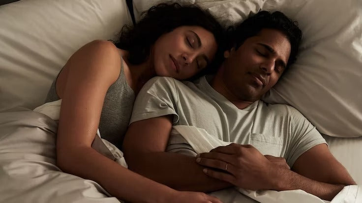 A couple sleeps, cuddling, in their bed.