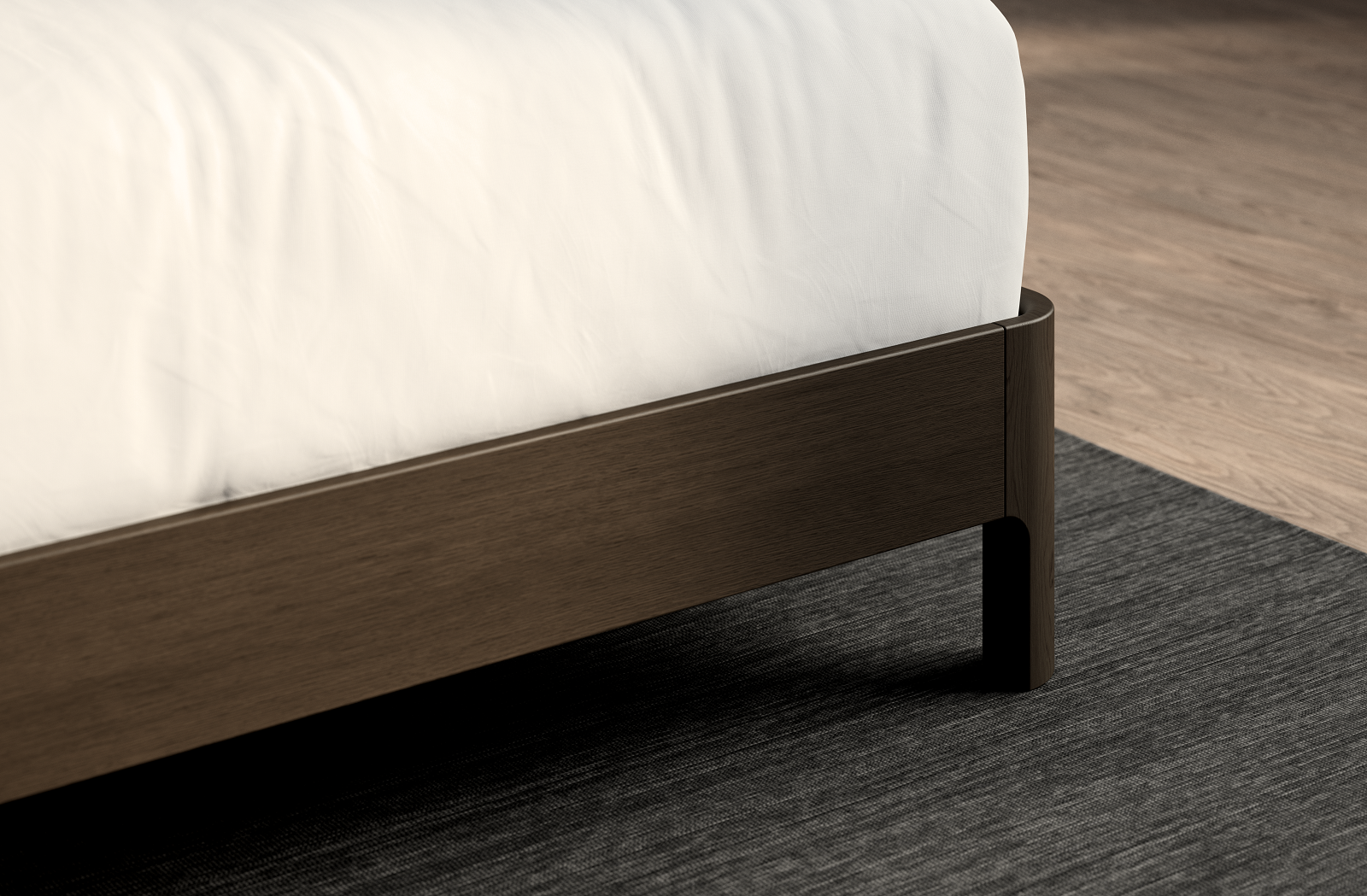  A close-up of a dark wood bed frame corner with a white mattress on top. The bed sits on a textured dark gray rug over a light wood floor.
