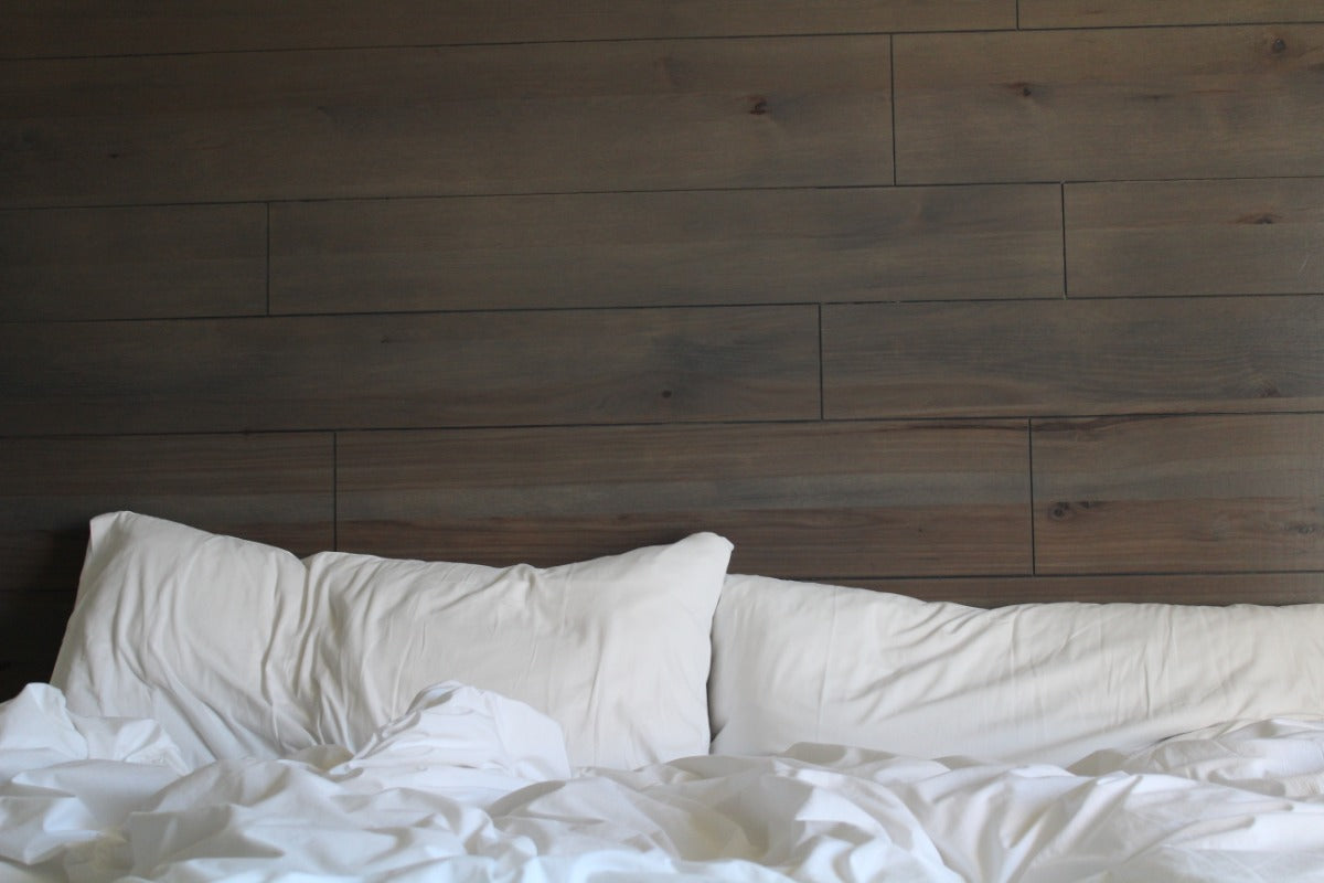  Close-up of two white pillows and rumpled white bedding against a dark brown wood plank headboard.