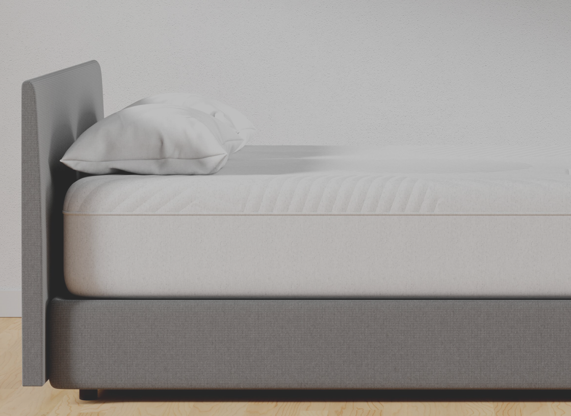  Close-up side view of a white mattress and pillows sitting on a gray upholstered platform bed frame.