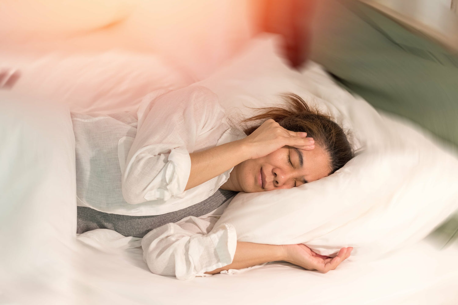 woman laying on her side in bed, touching her ear in pain