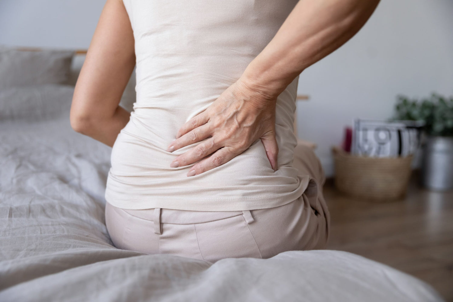 Old mature woman sitting on bed touching her back feeling morning back pain