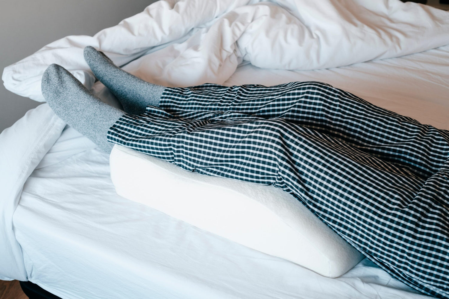 man in bed elevates his legs on a leg elevation pillow made of memory foam