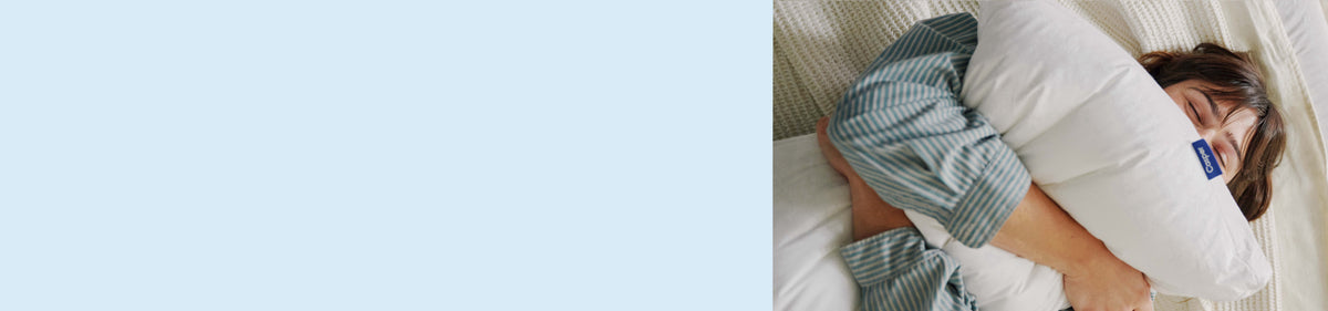 Light blue background. Image of a woman squeezing a pillow in bed.