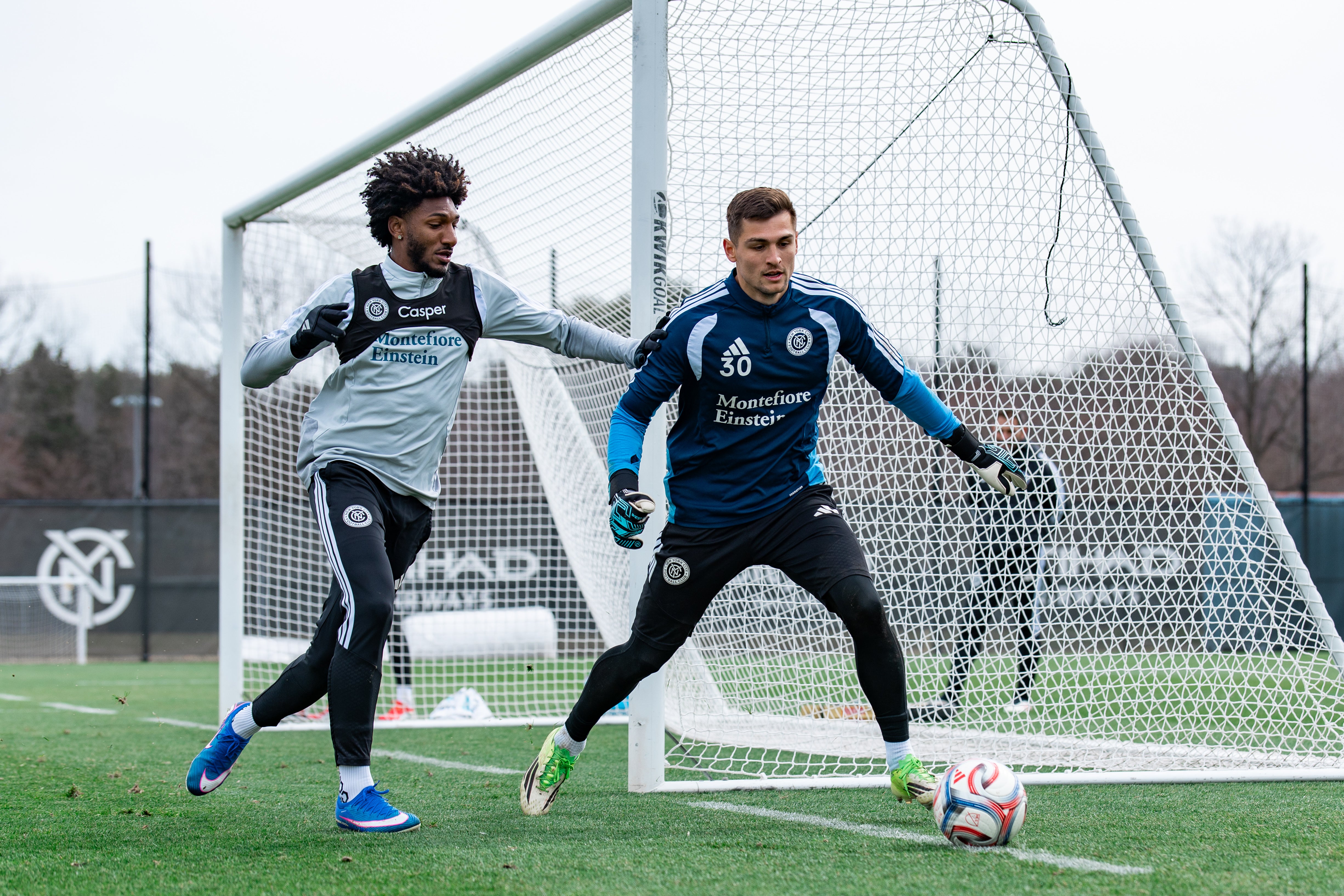 Two soccer players in training gear on a field with a goal in the background.