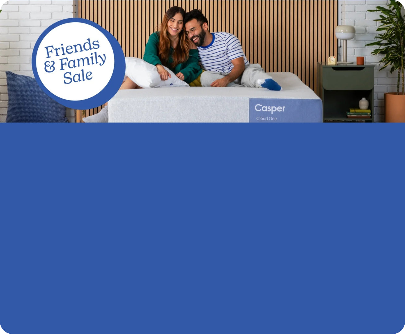 Two people sitting and smiling on their Casper Cloud One mattress against a wall with vertical wooden panels. On the image is a badge that reads "Friends and Family Sale"