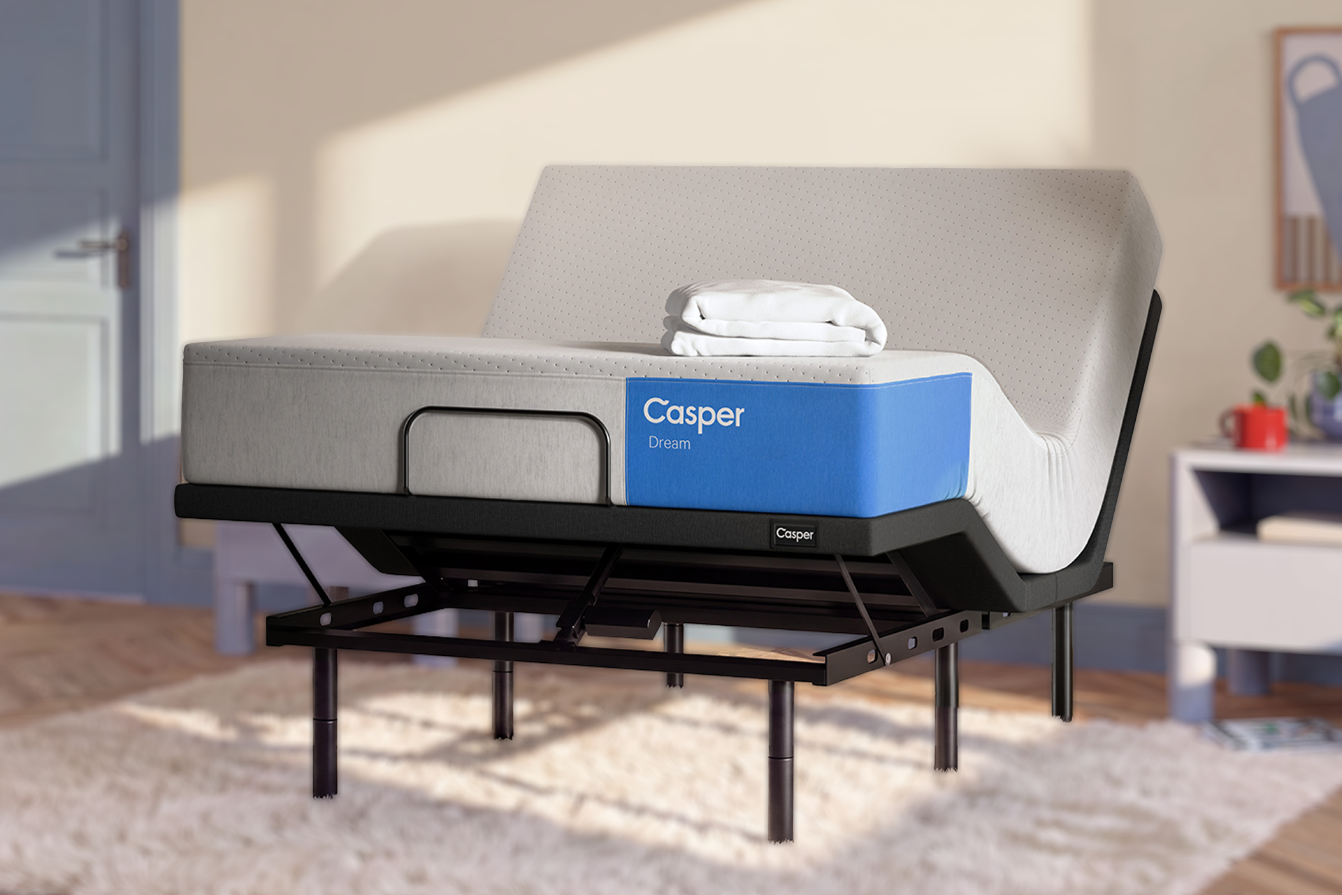 A Casper Dream mattress on a black adjustable bed frame, styled in a bright, modern bedroom setting with warm sunlight and shadows.