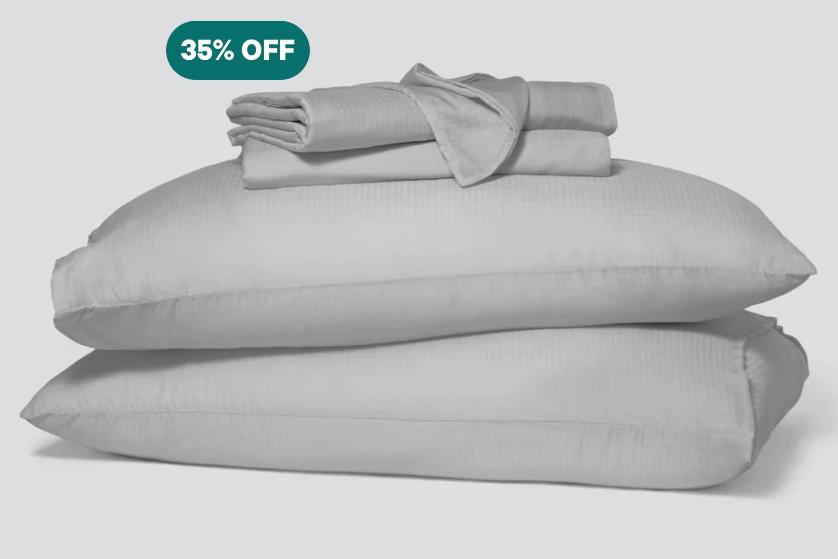 A stack of two pillows in gray pillowcases with a folded sheet set on top of them.