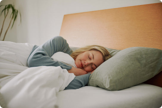 Woman sleeping peacefully on a bed with a green pillow and white blanket.