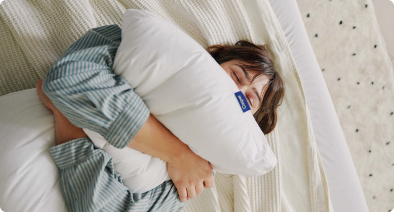 Aerial photo of a person lying on their back in bed, squeezing a pillow on their chest.