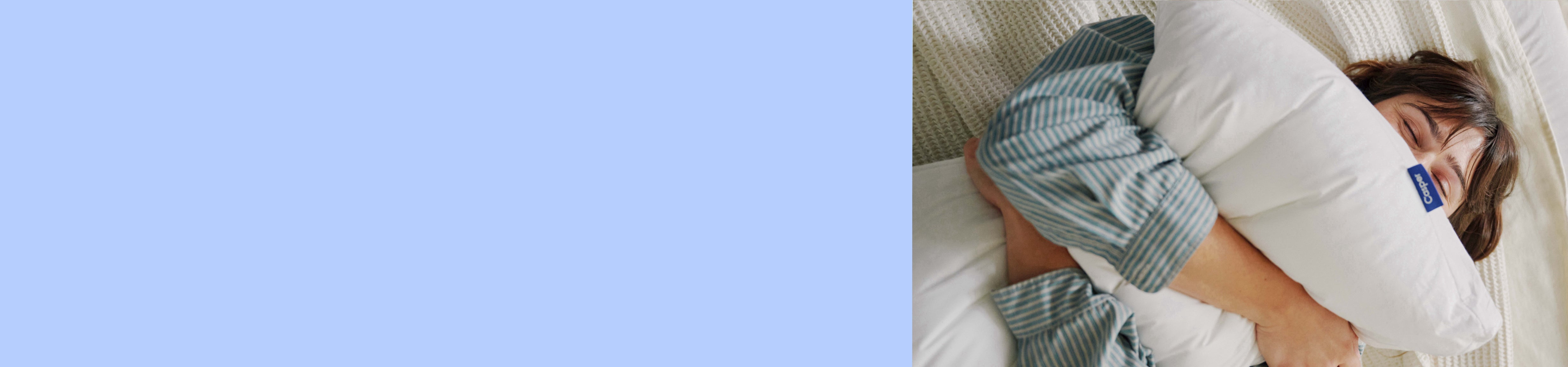 Light blue background. Image of a woman squeezing a pillow in bed.