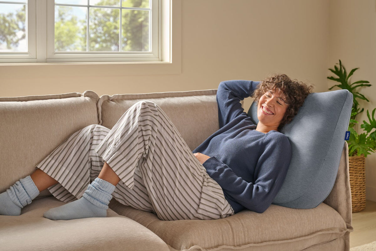 A woman leans back against the Backrest Pillow on a couch.