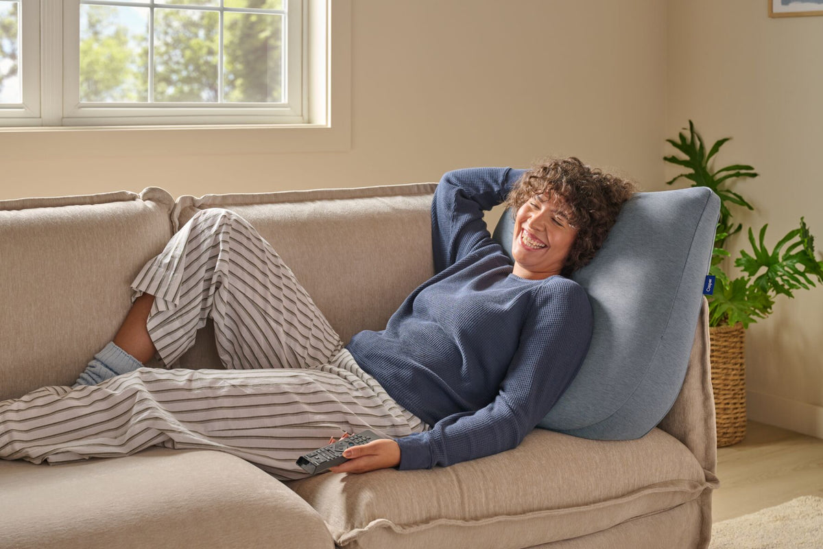 A woman leans back against the Backrest Pillow on a couch.