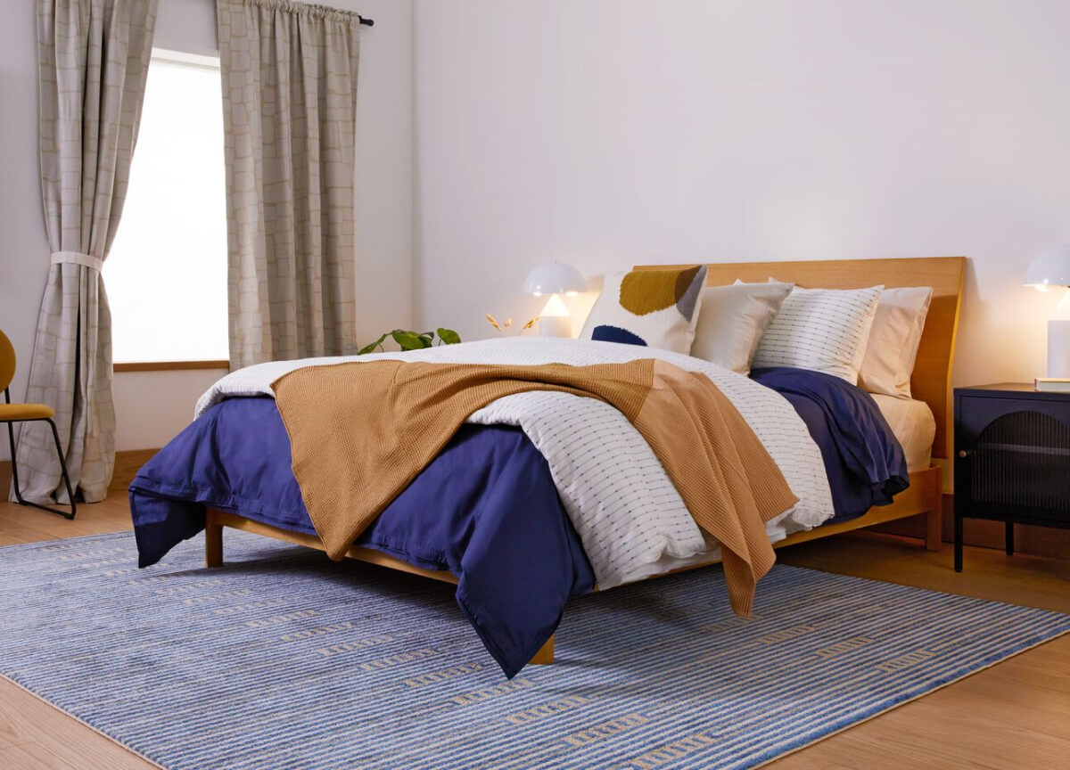 Bedroom with a bed covered in blue and brown blankets, white pillows, and a striped rug.