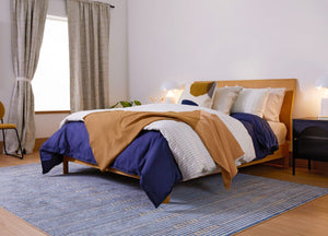 Bedroom with a bed covered in blue and brown blankets, white pillows, and a striped rug.
