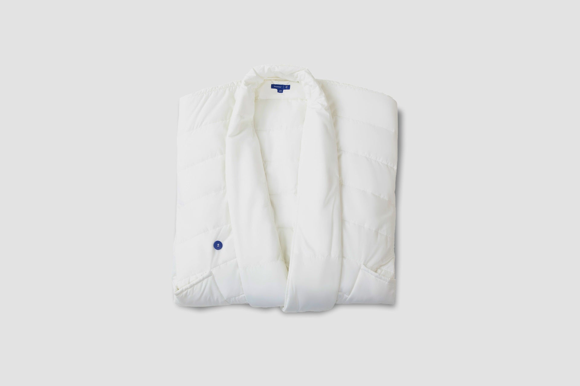 A folded, white Blanket Robe with a small blue button detail on the front, displayed against a solid light background