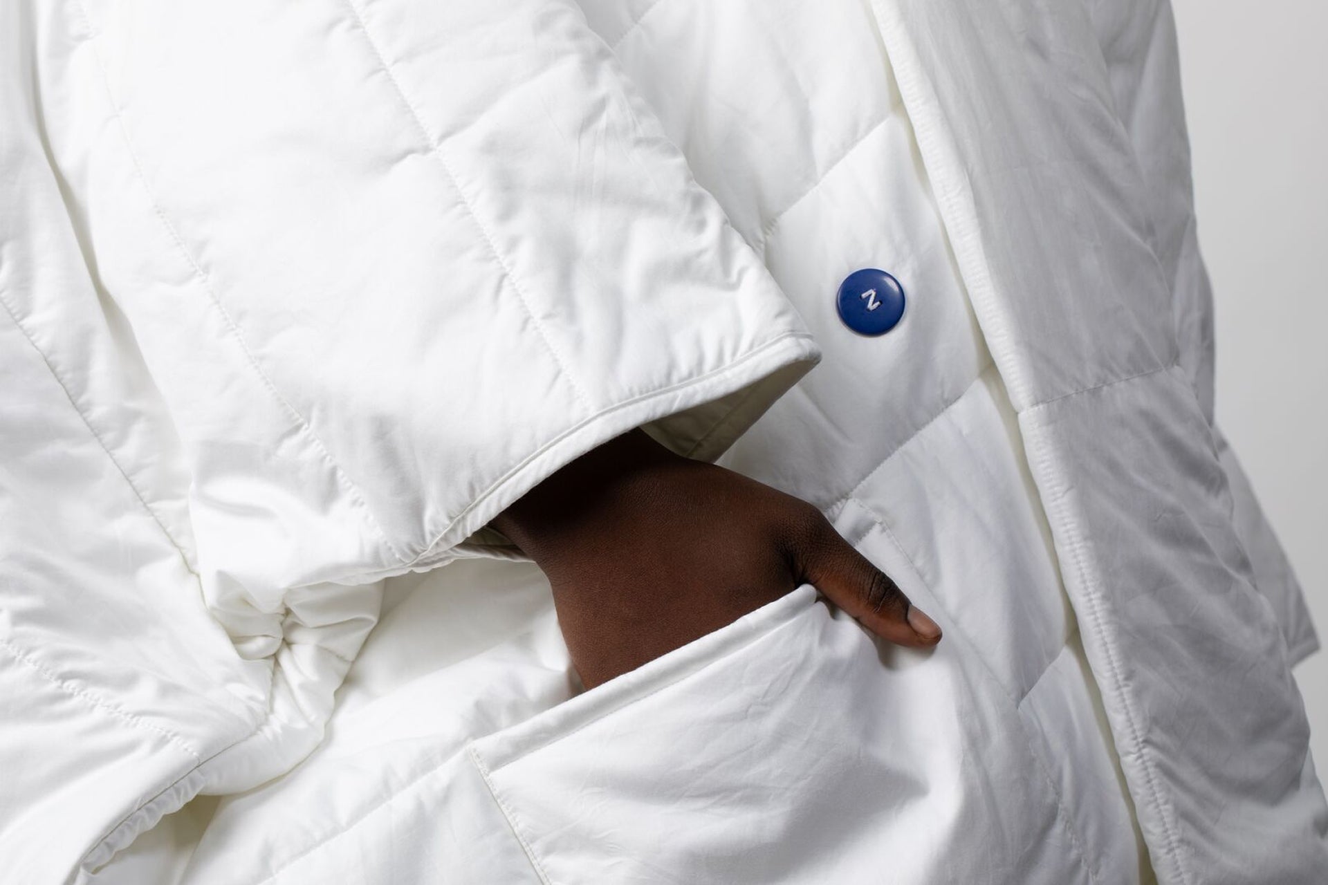 Close-up of a white Blanket Robe with a hand tucked into a front pocket, showing a small blue button detail