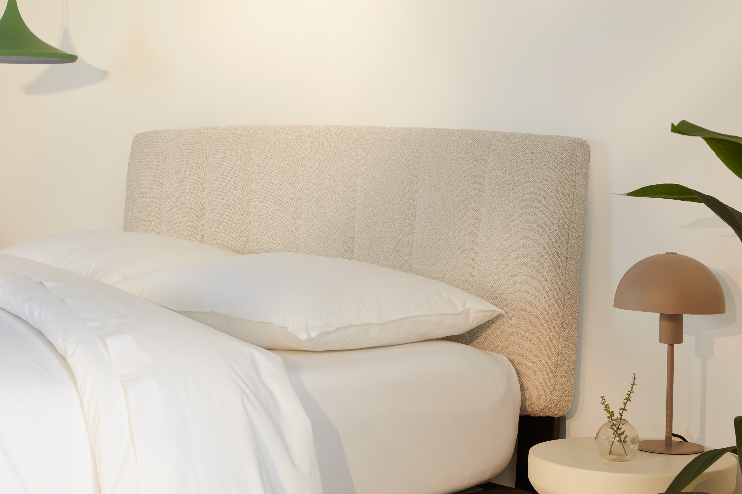 Neatly made bed with Bliss Attachable Headboard, cream color, and white bedding in a softly lit room.