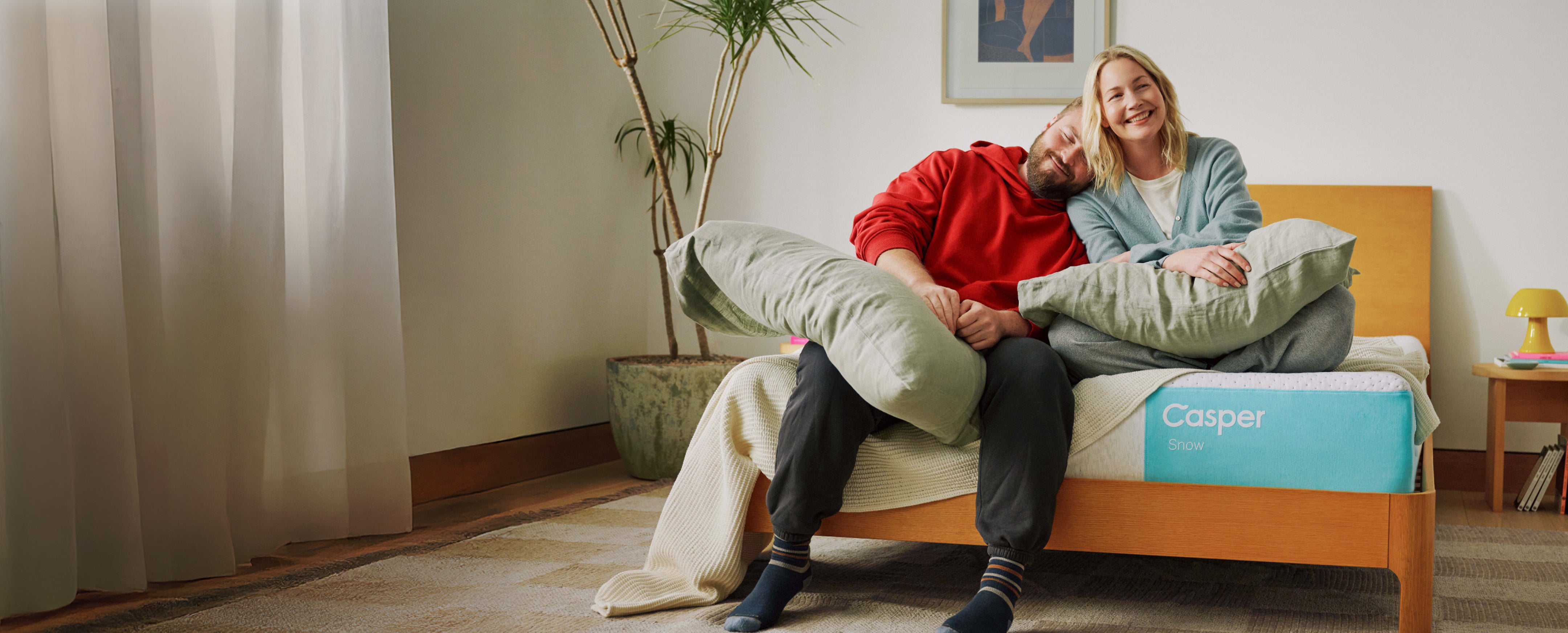 A couple sits happily on the edge of their Casper Snow mattress.