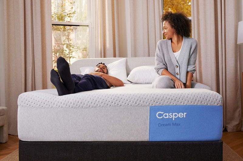A couple rests on their Casper Dream Max mattress, one lying down and the other sitting up. Front view image of bed.