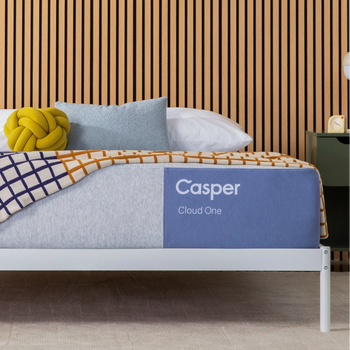 Casper's Cloud One mattress on a bed frame with pillows and a blanket folded on top