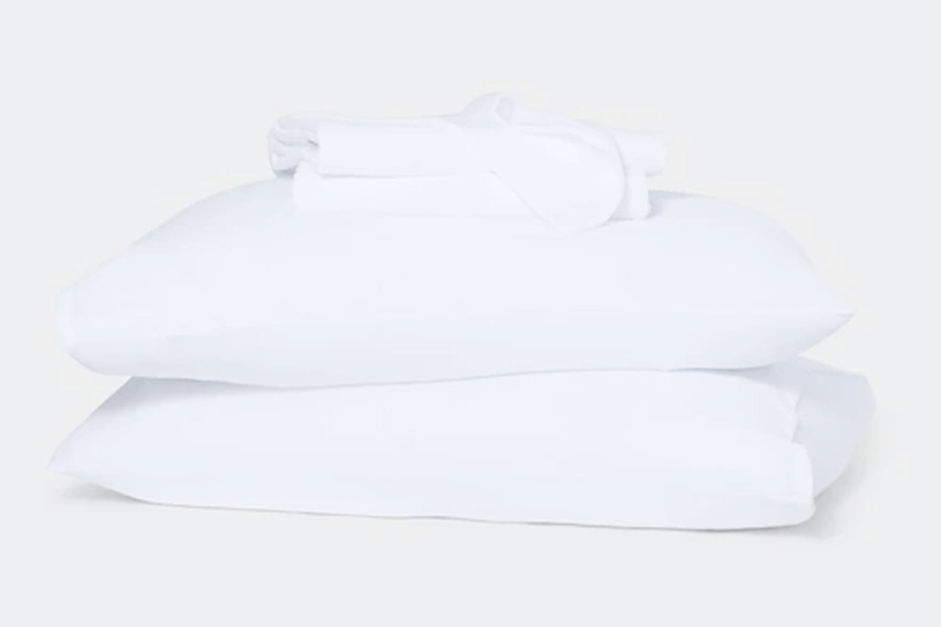 Stack of white sheet set, folded, on top of two pillows against a white background