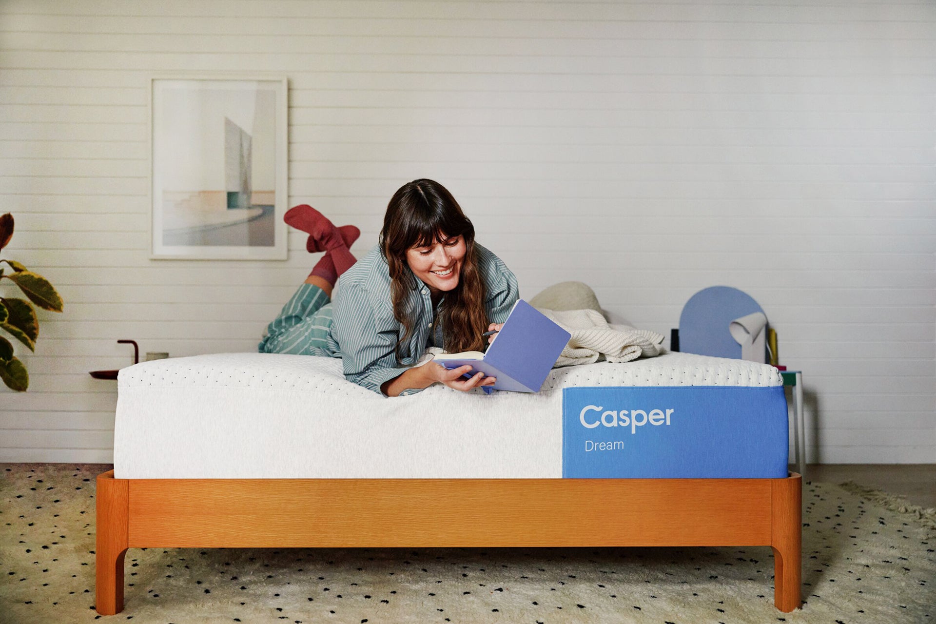 A woman lies near the edge of her Casper Dream Mattress with QuickCool™ Cover writing in a book.