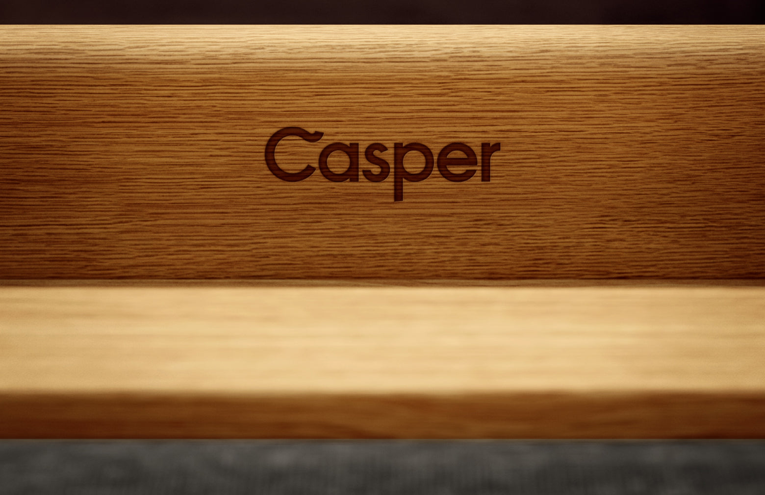 Close-up image of the front of a wooden bed frame that has the word "Casper" engraved on it