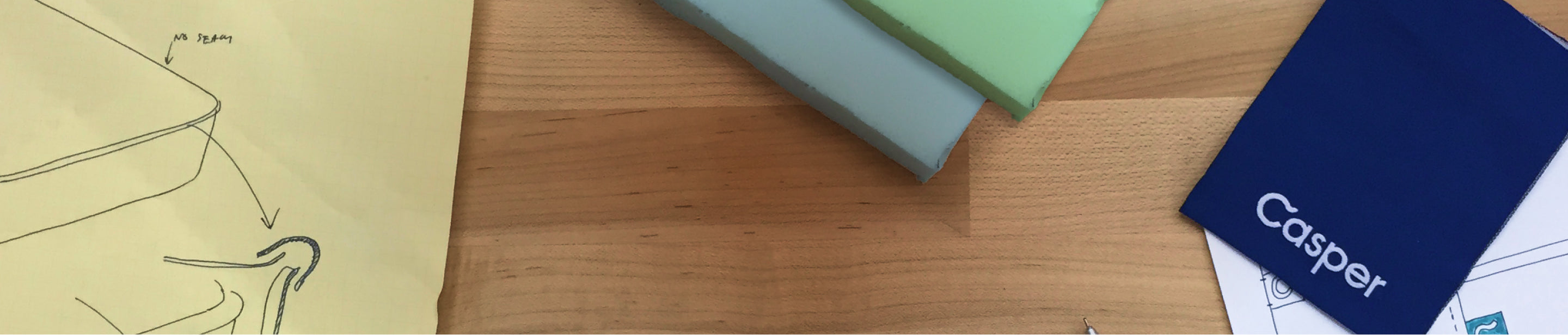 Wide-angle image of a work desk featuring a Casper manual and a paper with a hand-drawn illustration of a bed frame configuration