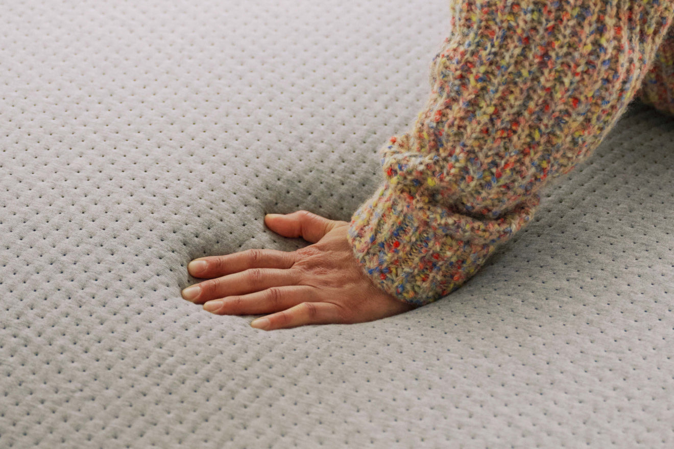 Close-up image of someone's hand pushing down on a mattress to feel it