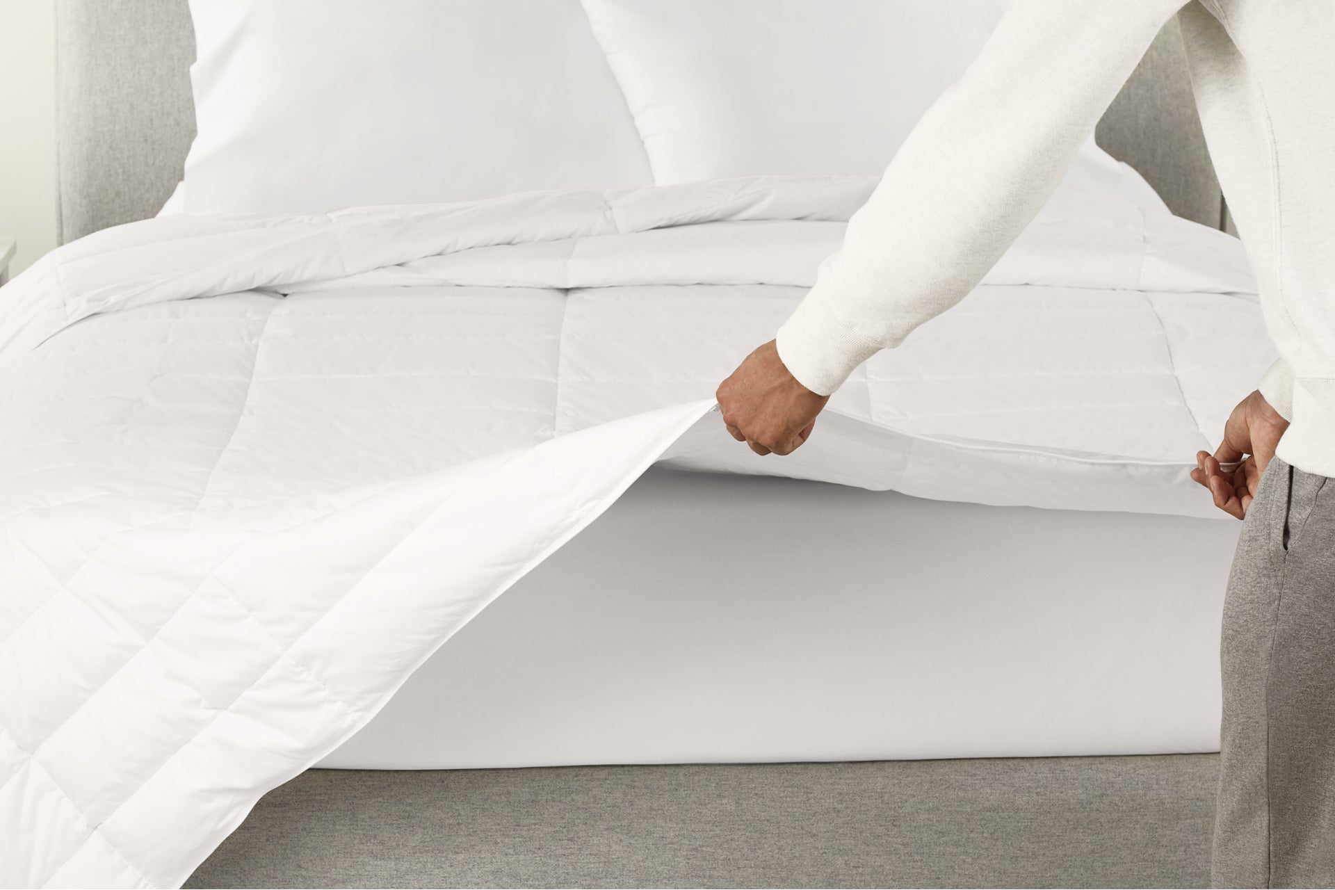 A person spreading the Down Duvet over a bed