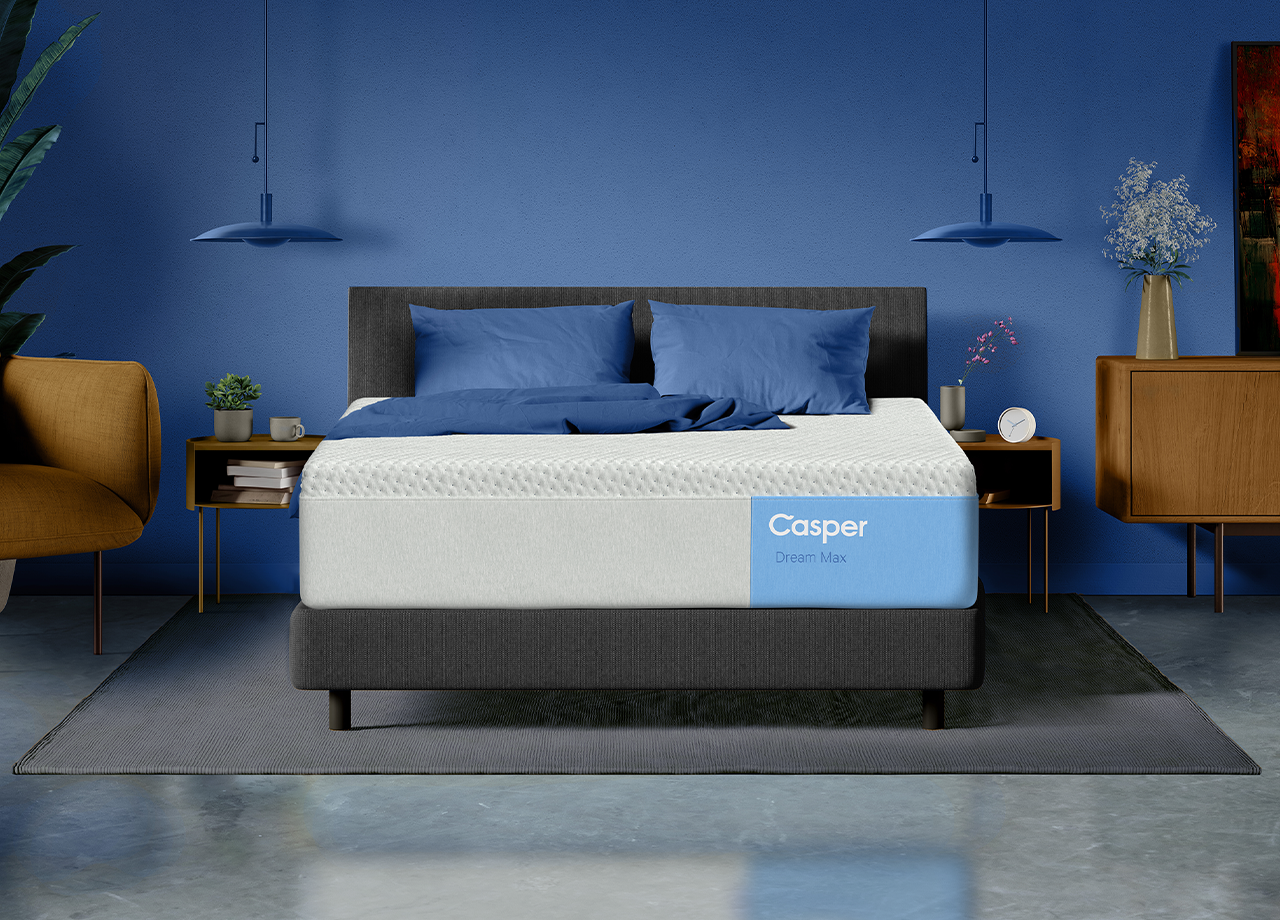 Front-facing view of the Casper Dream Max mattress on a bed frame in a bedroom with two pillows and a folded blanket laid on top of it.
