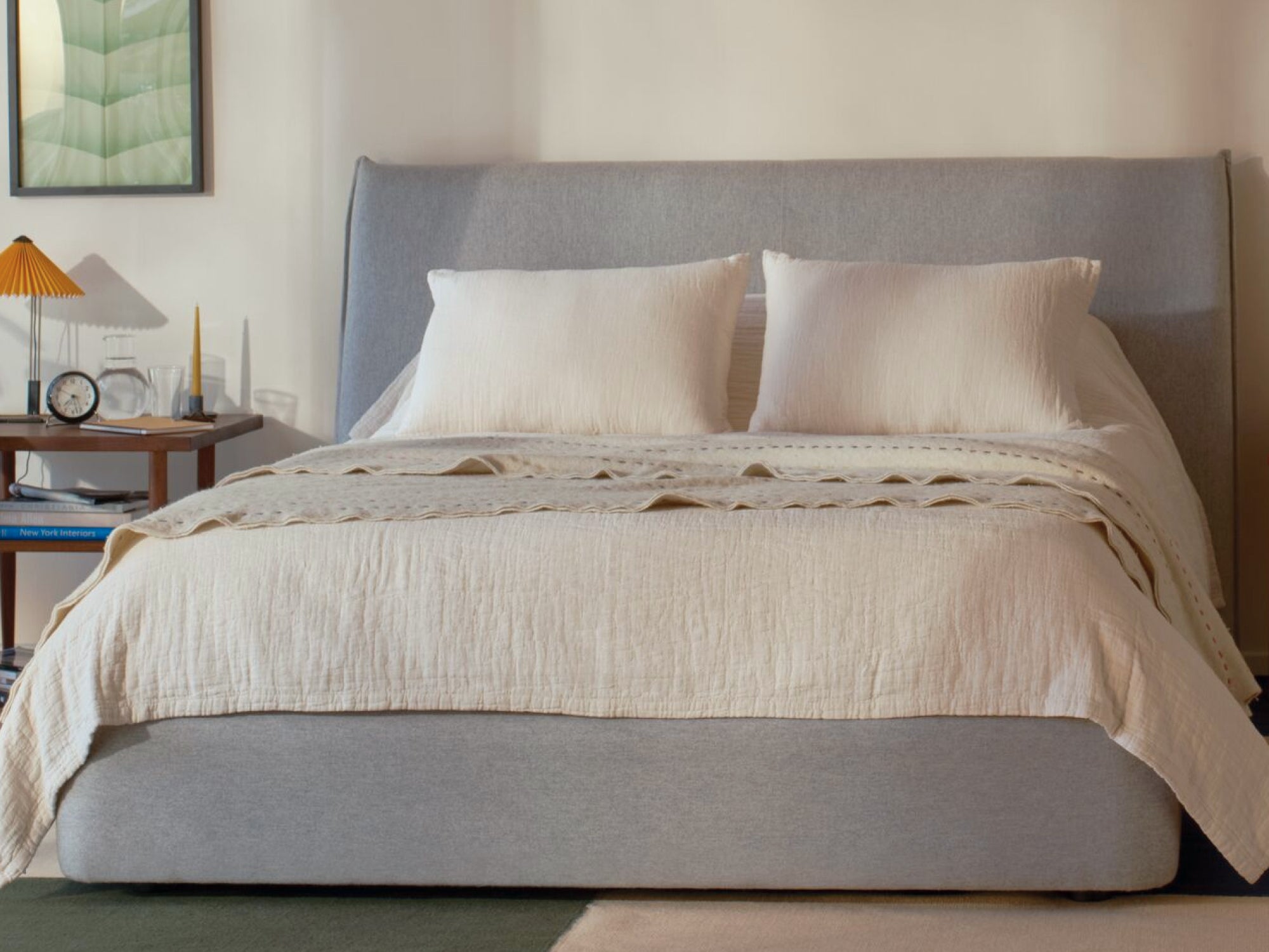 Front view of a fully made bed. The mattress is covered in a sheet and duvet with a blanket folded on top. There are multiple pillows on it, leaning against a headboard.