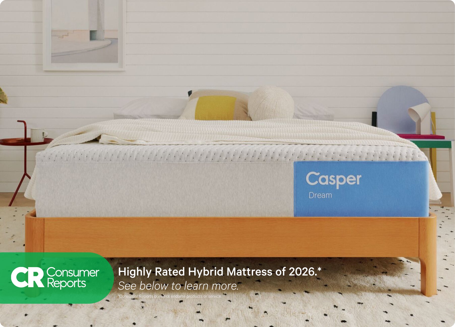 Front-view of the Casper Dream mattress on a wooden bed frame with pillows and a blanket folded on top. Beneath the image there appears a banner which says, "Consumer Reports. Highly rated hybrid mattress of 2026. See below to learn more. *Consumer Reports does not endorse products or service."