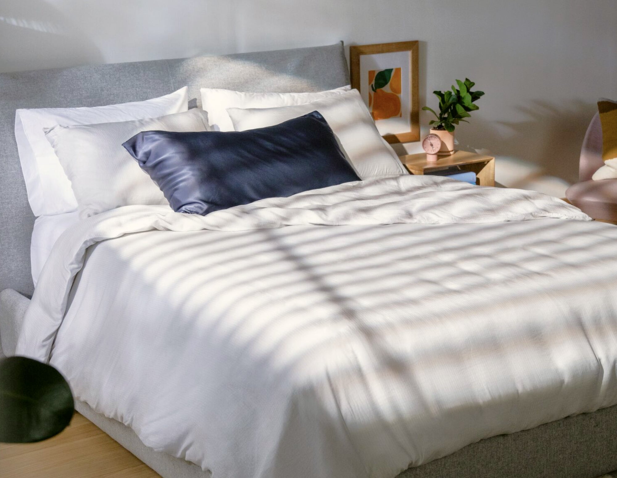 A corner view of a fully made bed. It has several pillows, a duvet, and he mattress is on top of a bed frame with a headboard behind it.