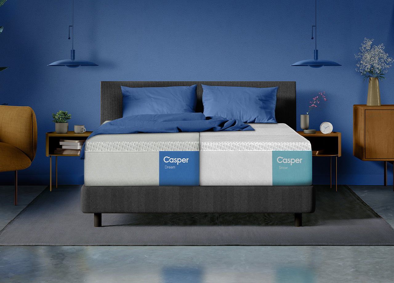 Front-facing view of a Split King bed frame with a different mattress on each half: the Casper Dream and the Casper Snow mattresses. On top of both mattresses are two pillows and a folded blanket laid on top.