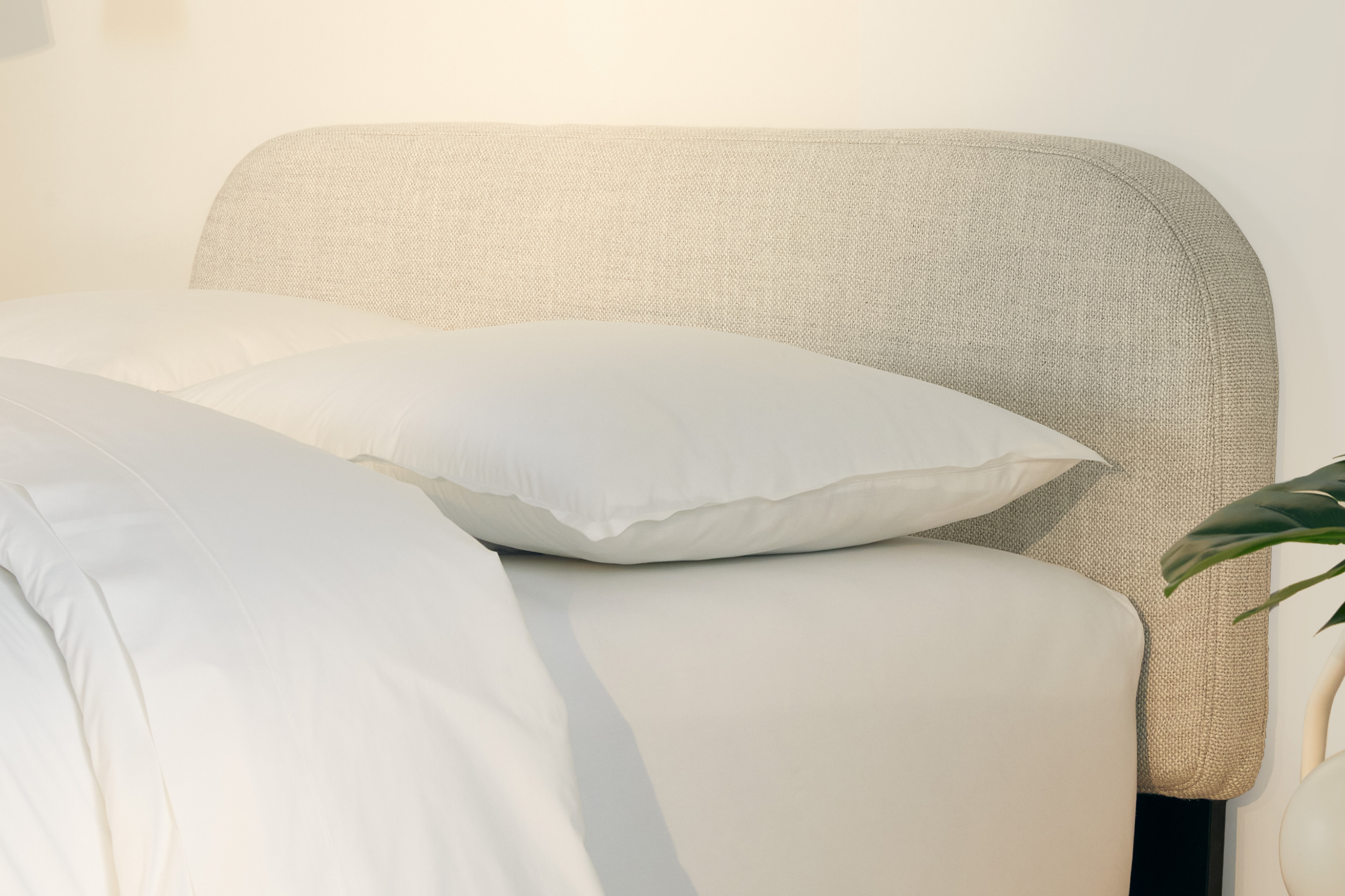 Neatly made bed with Drift Attachable Headboard, fog color, and white bedding in a brightly lit room.