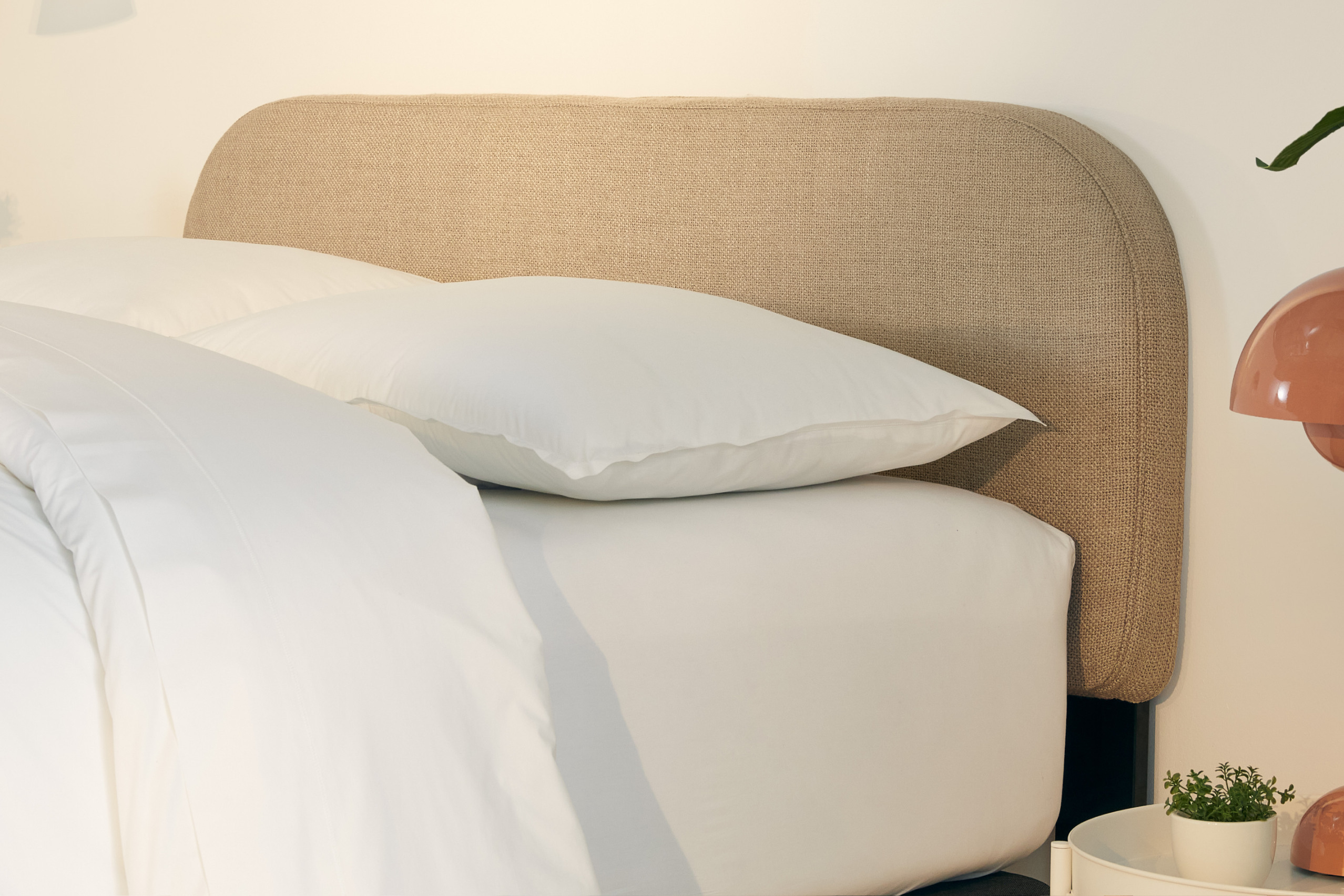 Neatly made bed with Drift Attachable Headboard, taupe color, and white bedding in a brightly lit room.