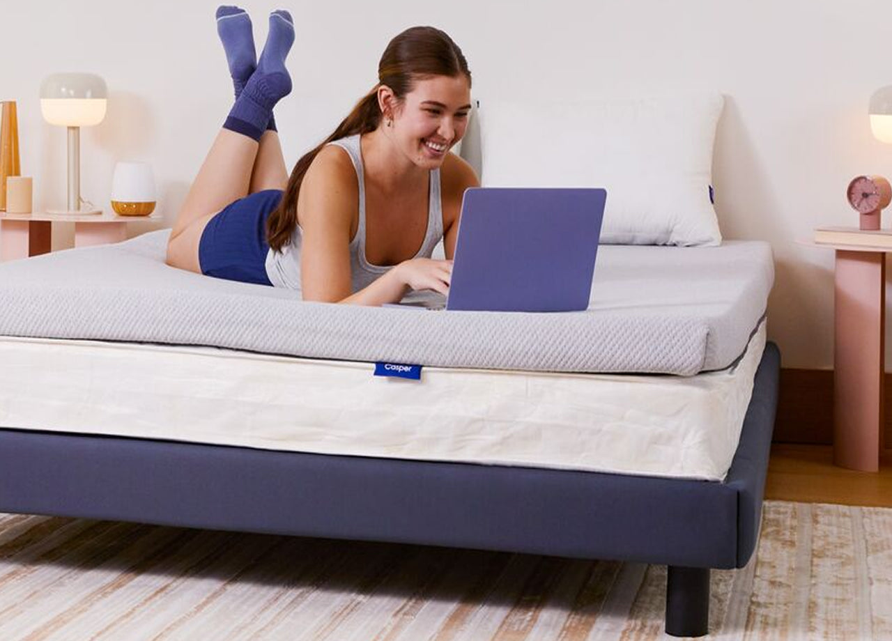 A person lies on her Essential Topper in bed with her laptop open.