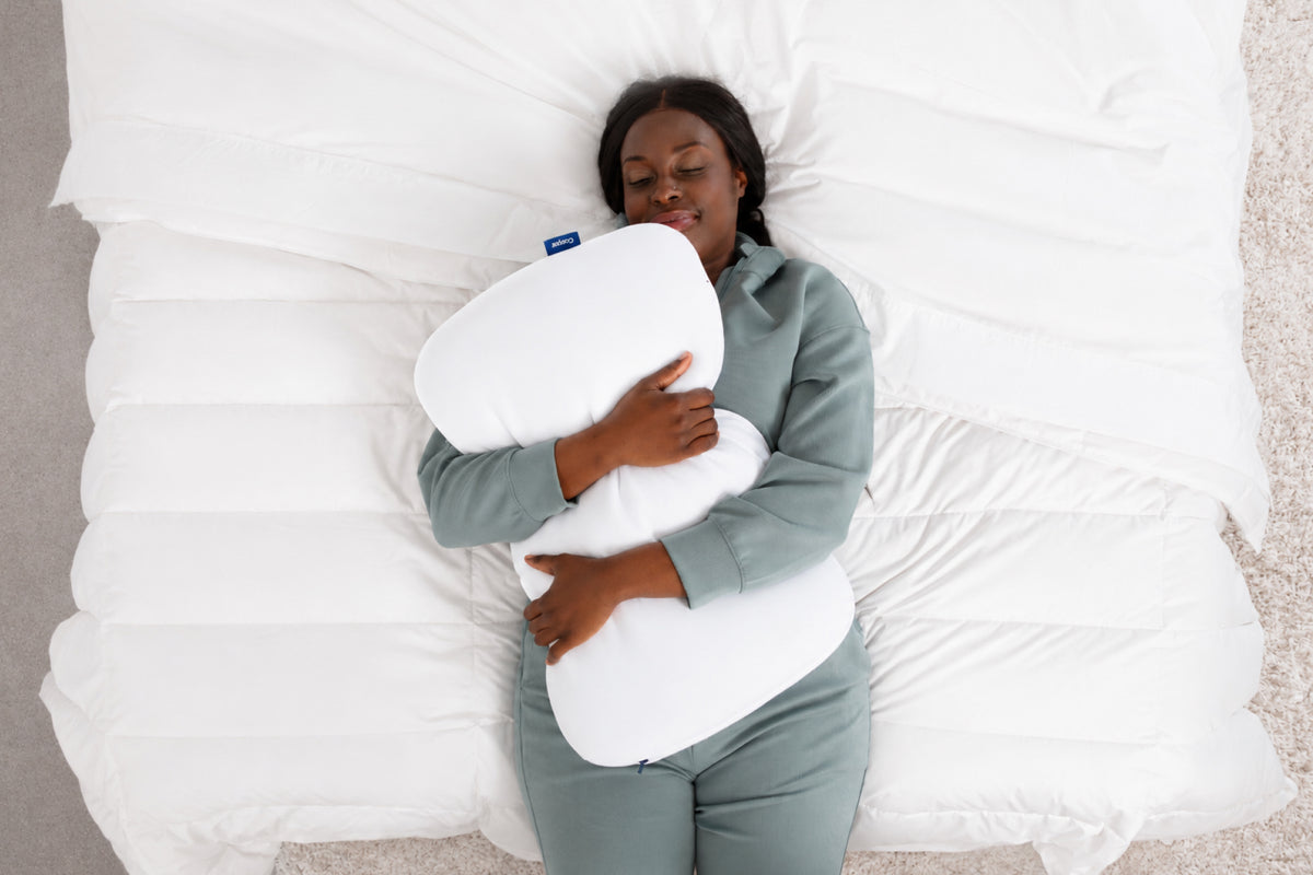 A woman lies in bed squeezing a Casper Foam Snow Pillow
