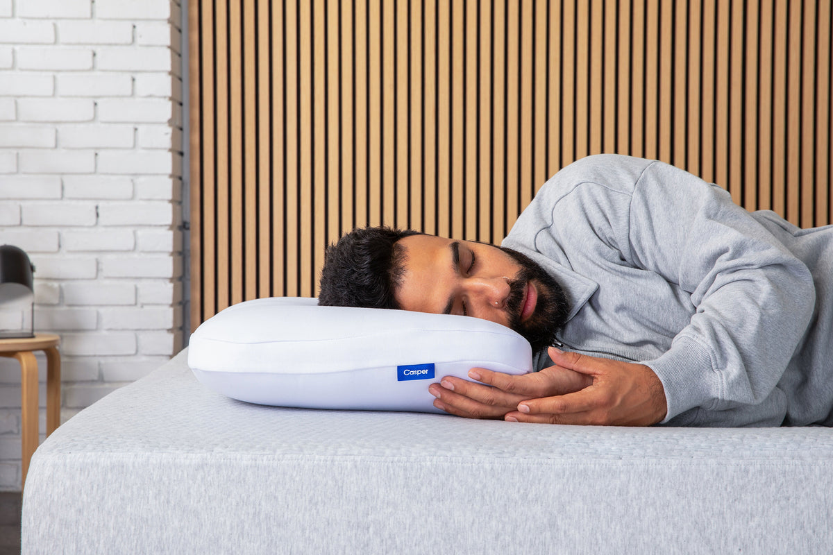 A man rests with the side of his head on Casper's Foam Snow Pillow.