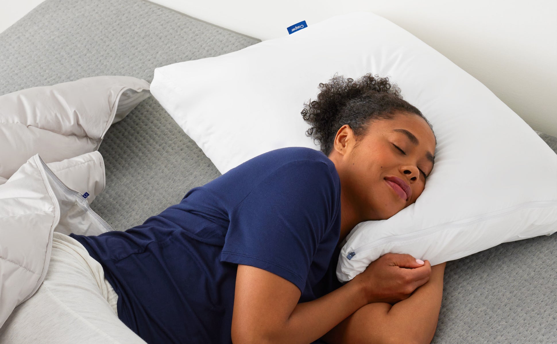 A person lies on their side with their head resting on the Casper Hybrid Pillow.