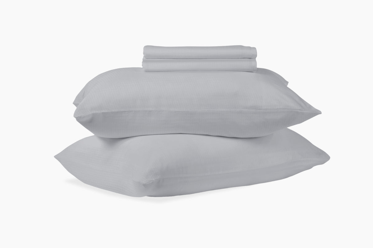 A stack of pillows and bed sheets, gray colorway, against a white background