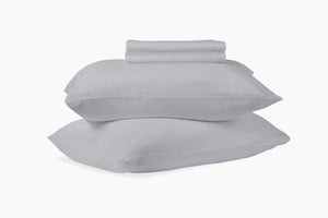 A stack of pillows and bed sheets, gray colorway, against a white background