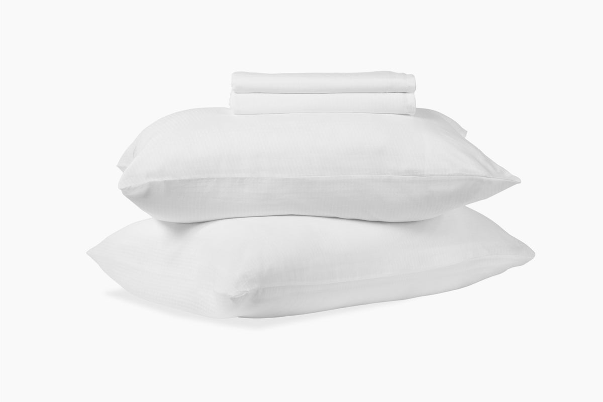 A stack of pillows and bed sheets, white colorway, against a white background