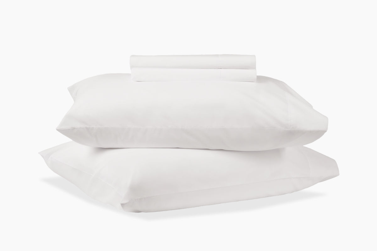 A stack of pillows and bed sheets, white colorway, against a white background